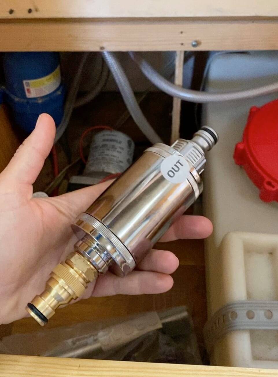 A person holding a Maunawai Campervan Waterfilter under a sink.