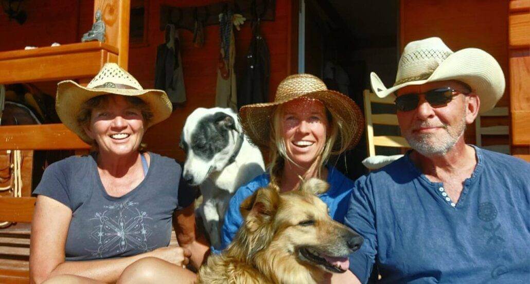 Three people and a dog in cowboy hats sitting on a porch.