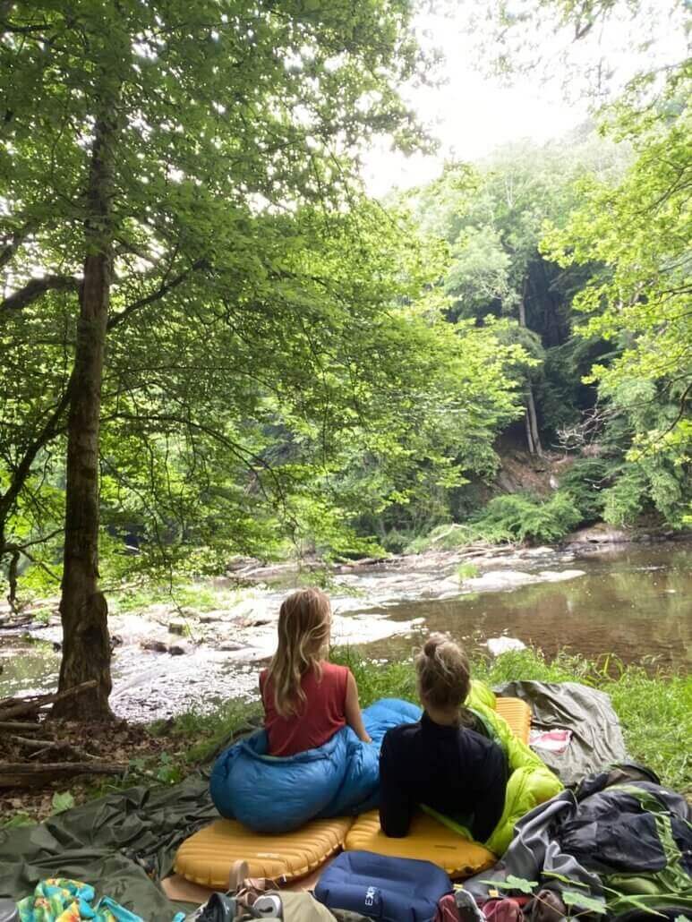 Two people sitting on the ground near a river.