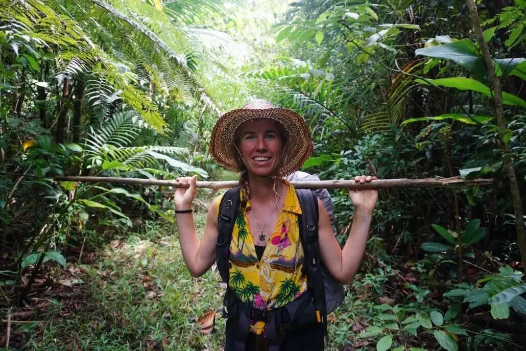 A woman wearing a hat and carrying a stick in the jungle.