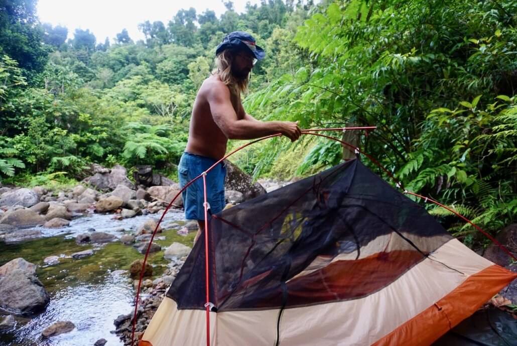 A man is setting up a tent near a stream.