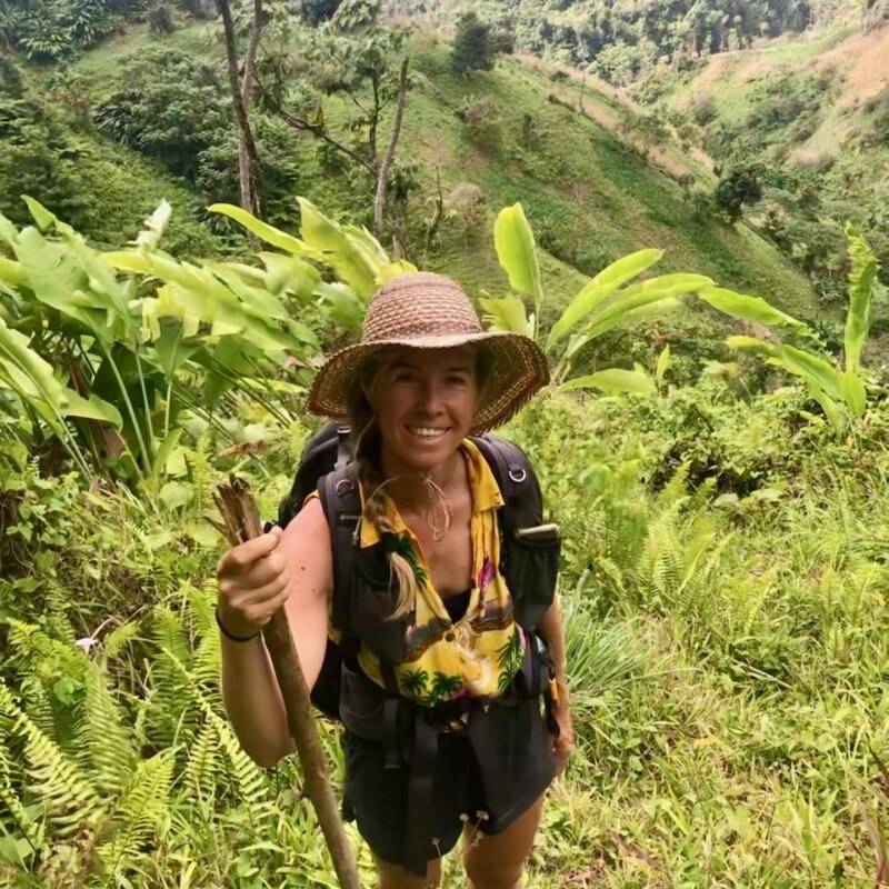 A woman wearing a hat and a backpack on a trail.
