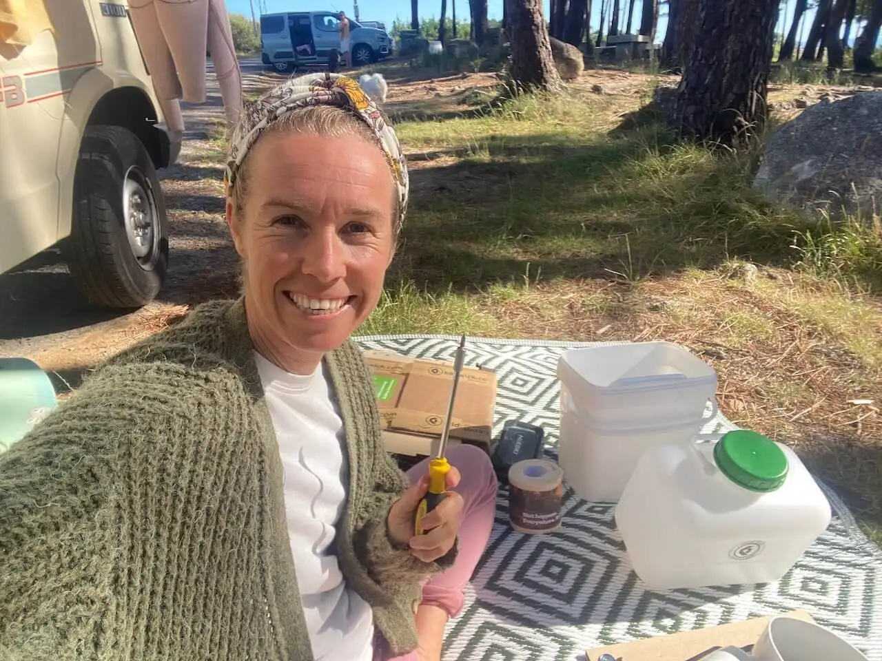 Me sitting on a picnic blanket outside the van with camping gear around me