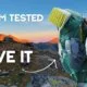 A woman with a large hiking backpack stands on a rocky mountain trail at sunset. Text reads: "850 KM TESTED. LOVE IT BUT....