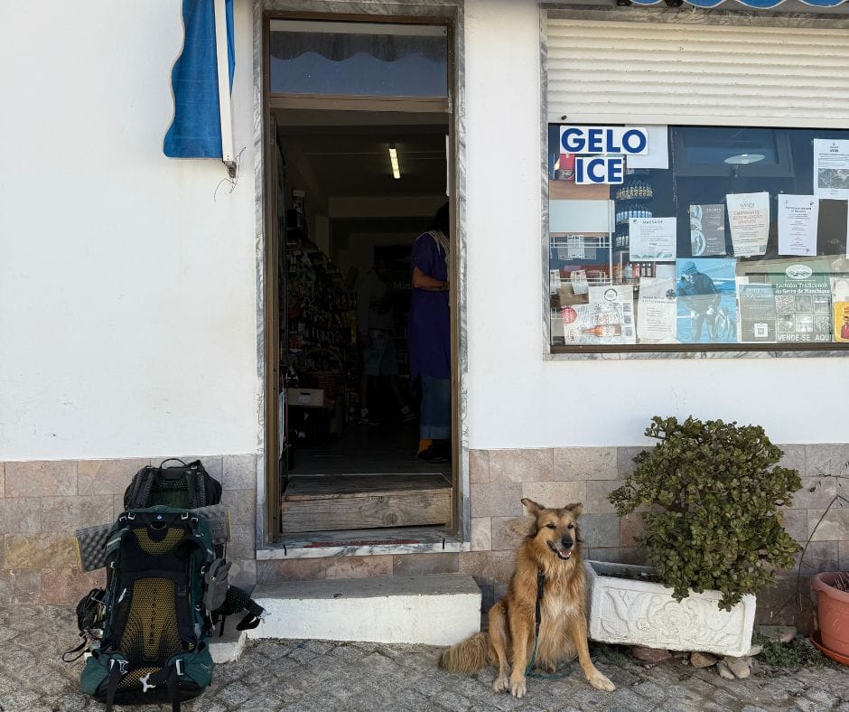 Wingo the dog resting next to a backpack outside a village shop on the Fisherman's Trail.