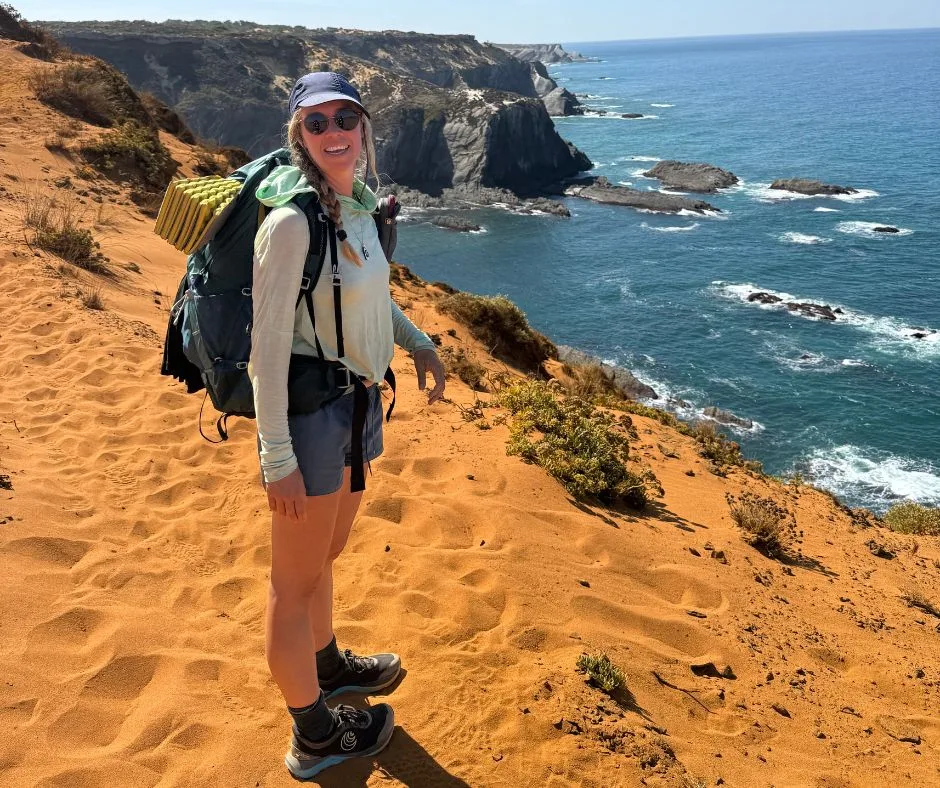 Hiker with backpack standing on a sandy cliff on the Fisherman's Trail overlooking the Atlantic.