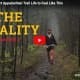 A person wearing a cap and hiking gear walks on a rocky forest trail, surrounded by leafless trees and green moss, with text reading "The Reality Chapter 2.
