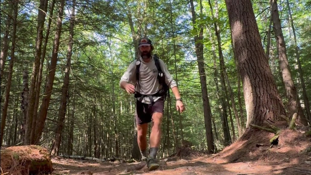 A hiker moving fast down a muddy Appalachian Trail section with exposed roots and brown earth