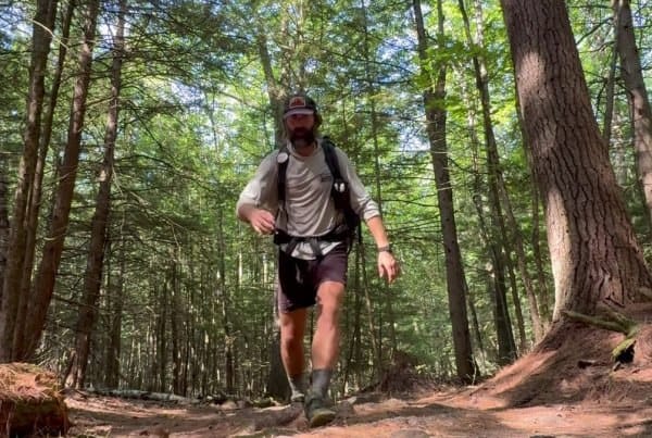 A hiker moving fast down a muddy Appalachian Trail section with exposed roots and brown earth