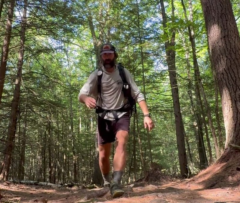 A hiker moving fast down a muddy Appalachian Trail section with exposed roots and brown earth