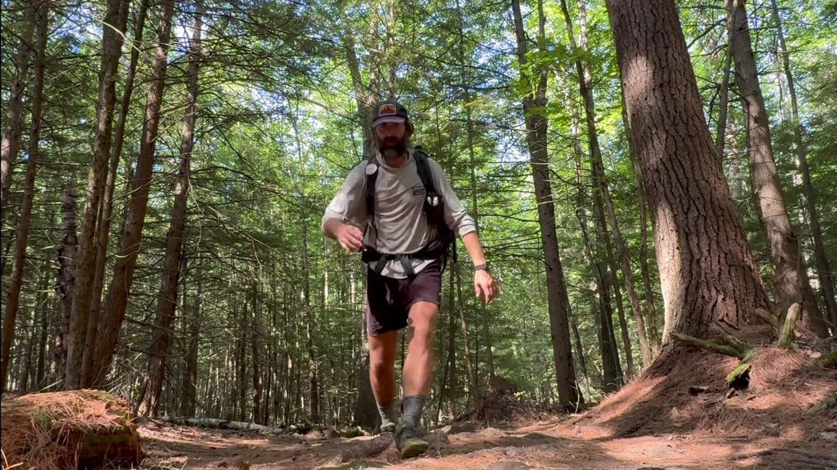 A hiker moving fast down a muddy Appalachian Trail section with exposed roots and brown earth