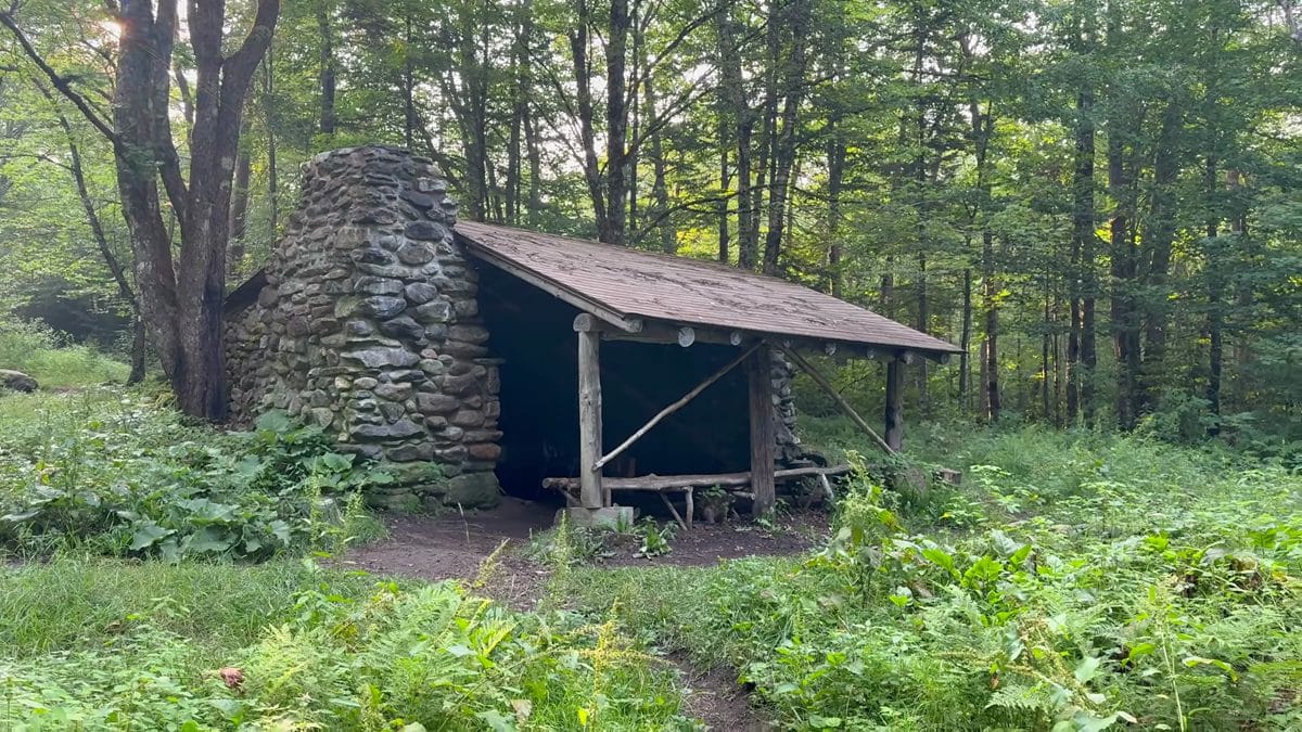 A rustic Appalachian Trail three-sided shelter with stone chimney nestled in a forest clearing