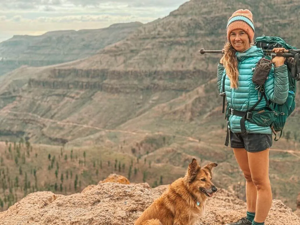 Me in my teal jacket and beanie on a rocky cliff on the GR11 with my dog