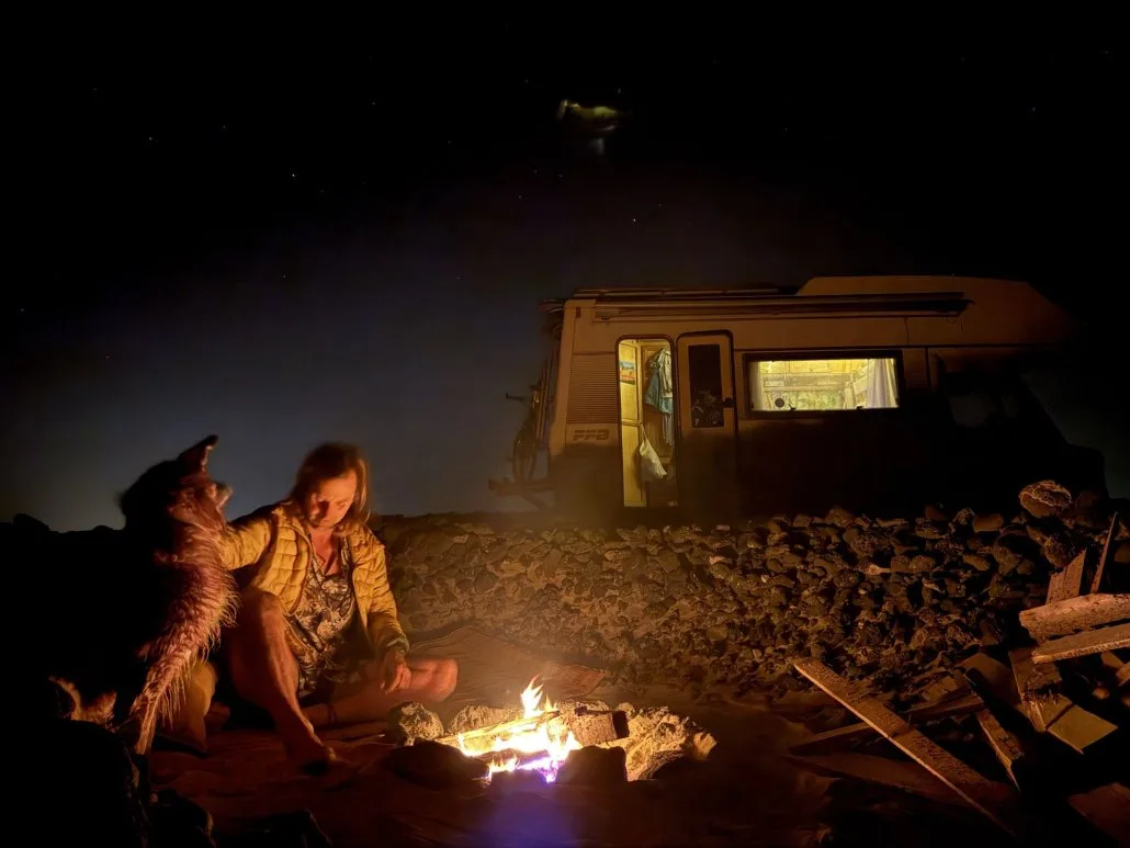 A campfire on the beach at night with Wingo and the van under the stars