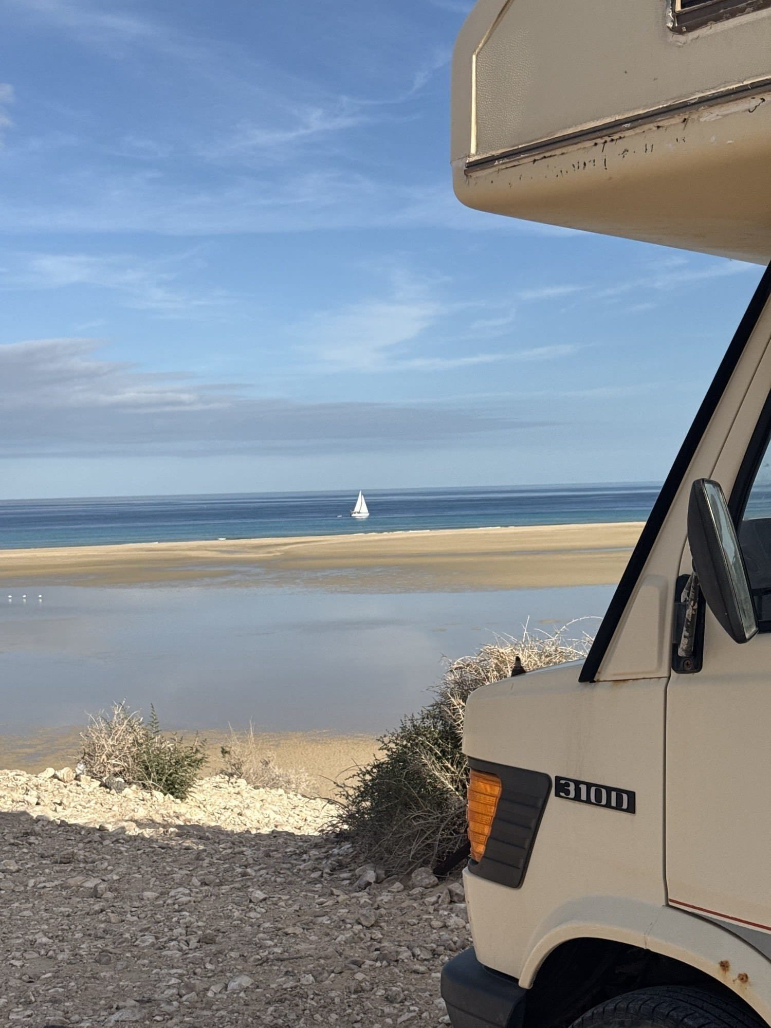 View from the camper on Fuerteventura: turquoise lagoon, sandbar and a small sailboat at anchor.