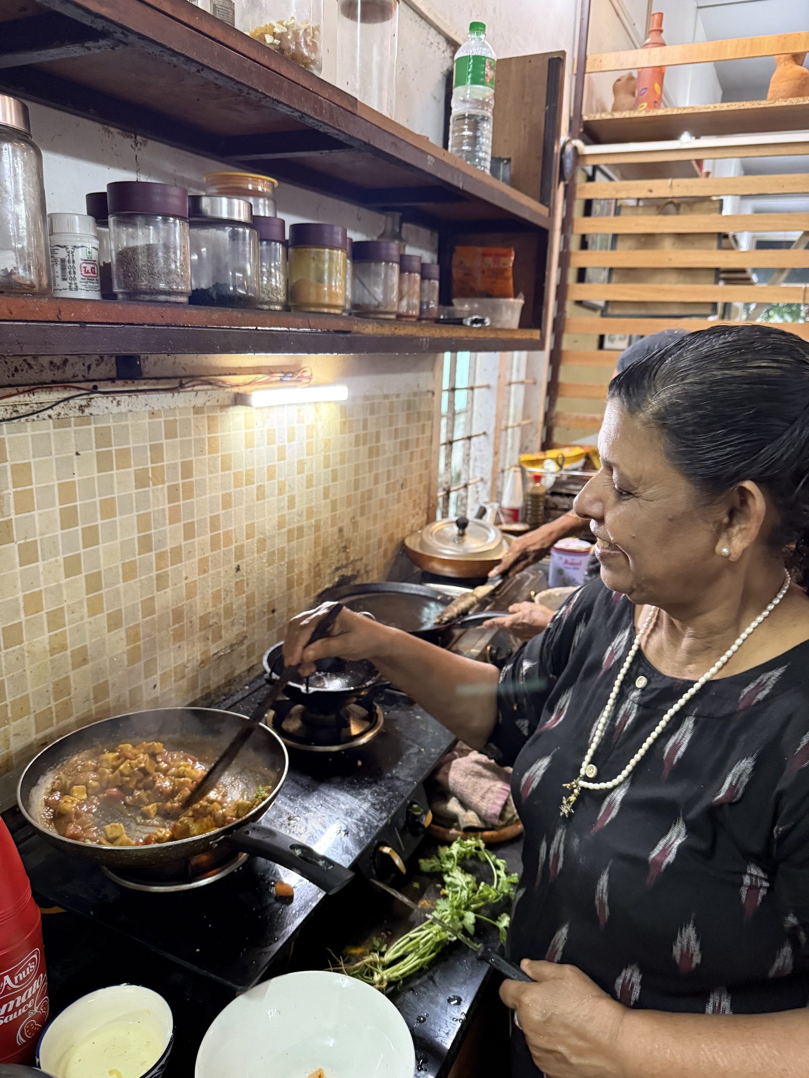 A Kerala cook stirring a pan in a small kitchen, teaching Ayurvedic cooking