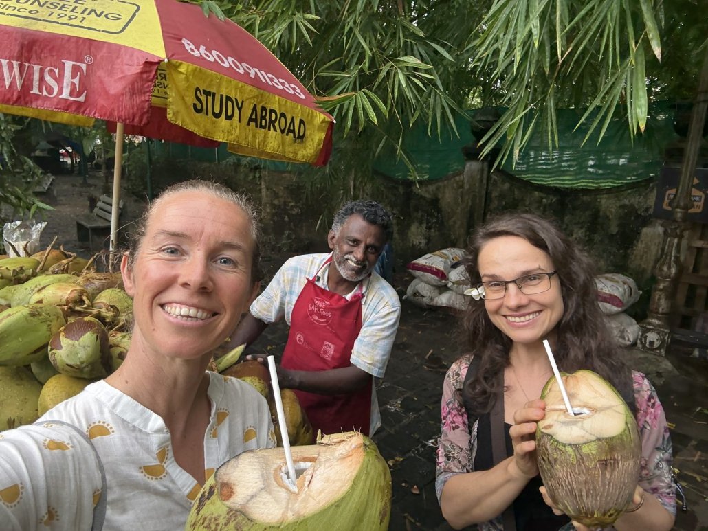 Suzanne and two fellow travellers drinking fresh coconuts at a roadside stall in Kerala
