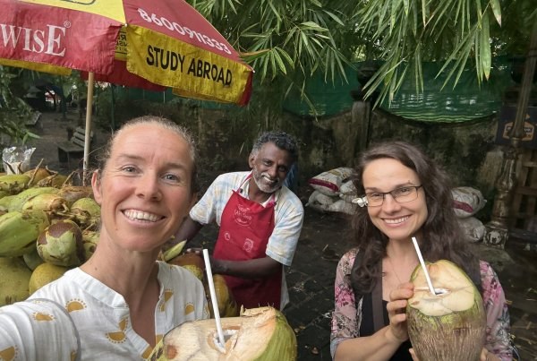 Suzanne and two fellow travellers drinking fresh coconuts at a roadside stall in Kerala
