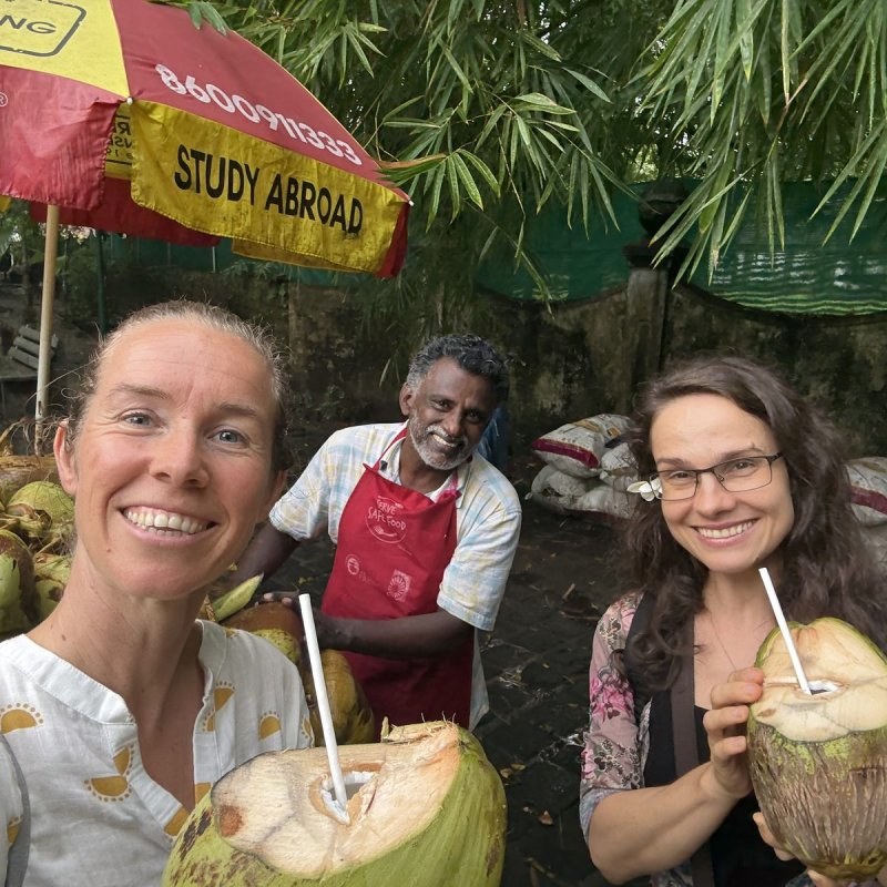 Suzanne and two fellow travellers drinking fresh coconuts at a roadside stall in Kerala
