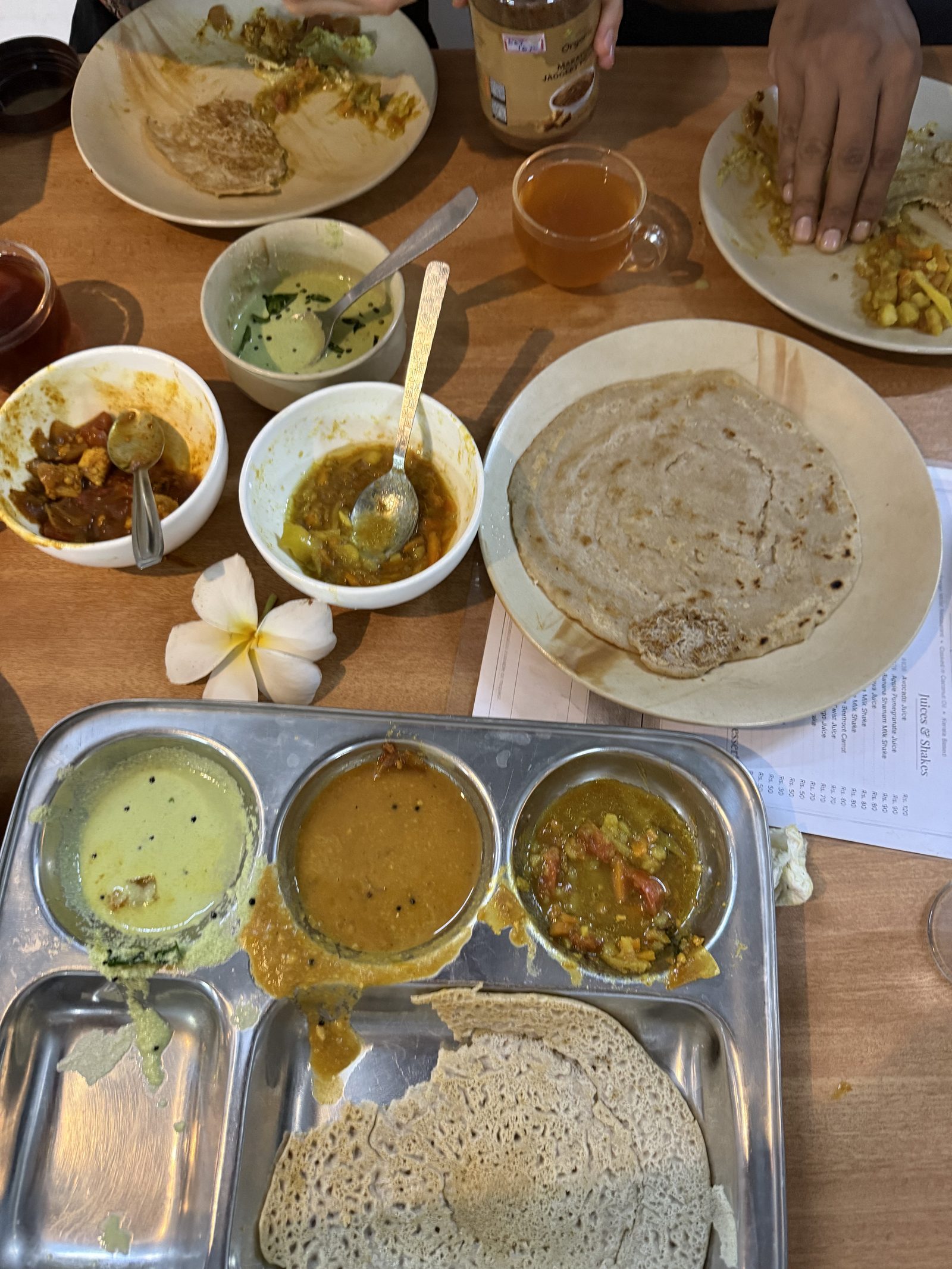 A Kerala vegetarian meal on steel plates: dosa, sambar, curries, chutney and a frangipani flower