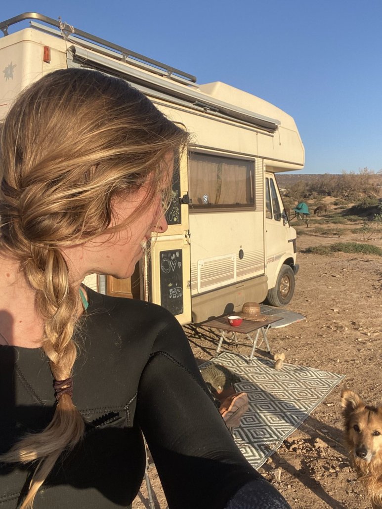 Suzanne in her wetsuit next to her old Mercedes camper van, with Wingo the dog